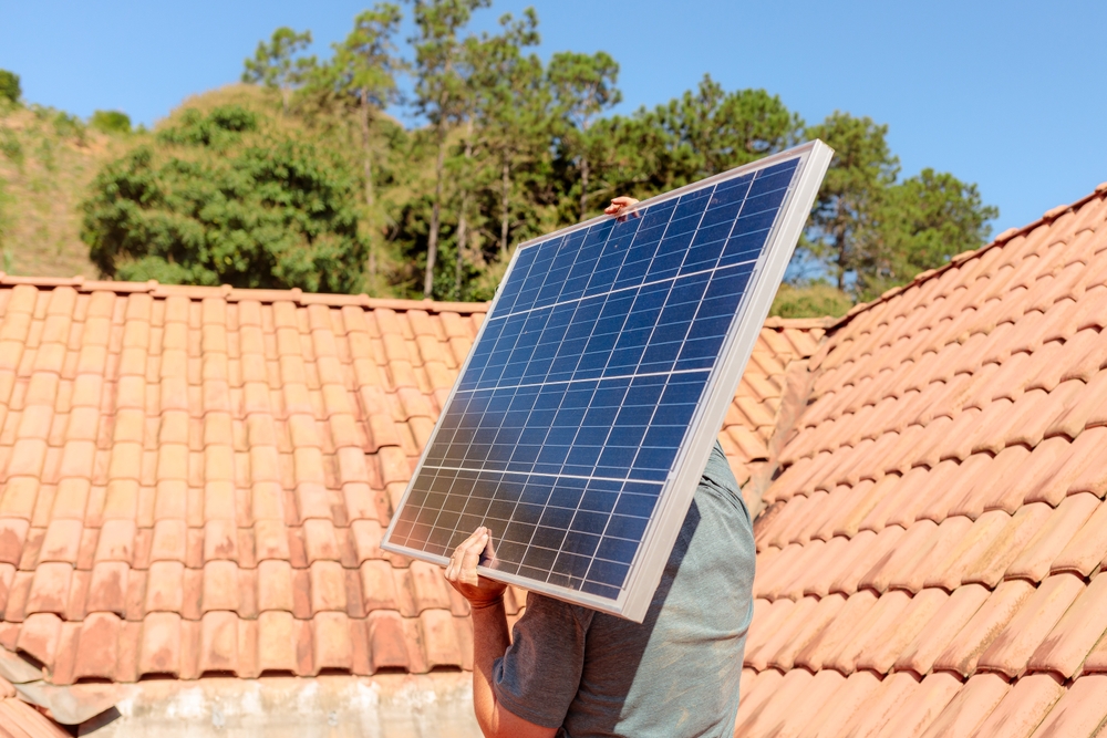 Technician,Carrying,A,Solar,Panel,On,A,Residential,Roof,Under